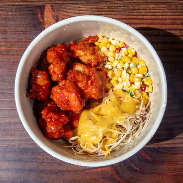 Mr. Dak's Korean fried chicken with red sauce, corn, shredded cabbage, and yellow dressing in a bowl.