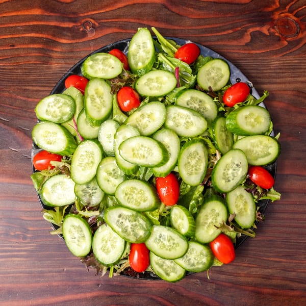 Overhead view of a fresh salad with sliced cucumbers, cherry tomatoes, and mixed greens.