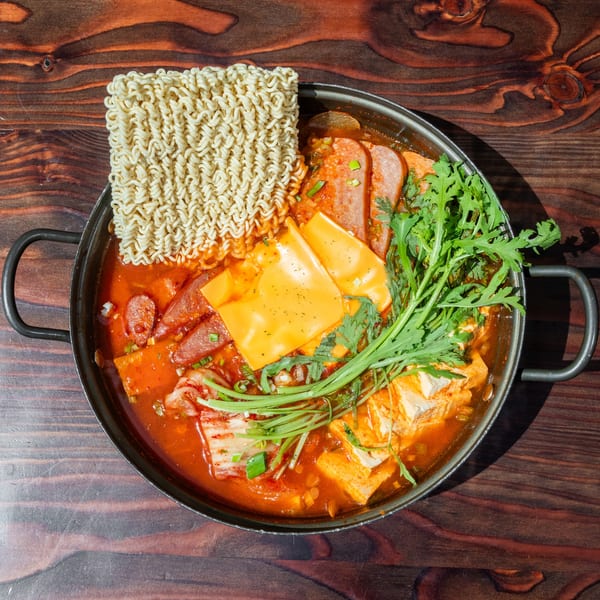 Top-down view of Mr. Dak's Korean budae jjigae with ramen, spam, cheese, and greens.
