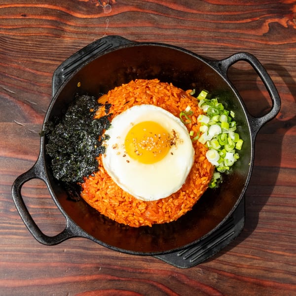 Mr. Dak's kimchi fried rice with a fried egg, seaweed, and green onions in a black skillet.