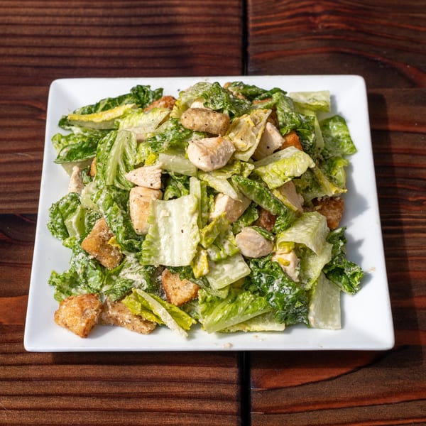 A Mr. Dak Caesar salad with chicken, croutons, and dressing on a white plate.