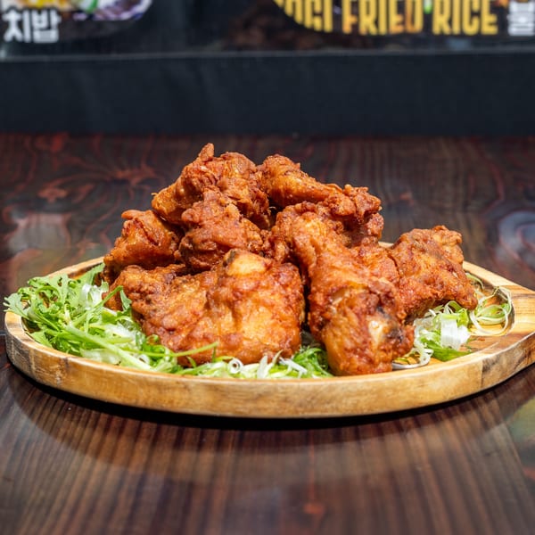 Crispy Korean fried chicken pieces on a wooden platter with fresh green lettuce and scallions.