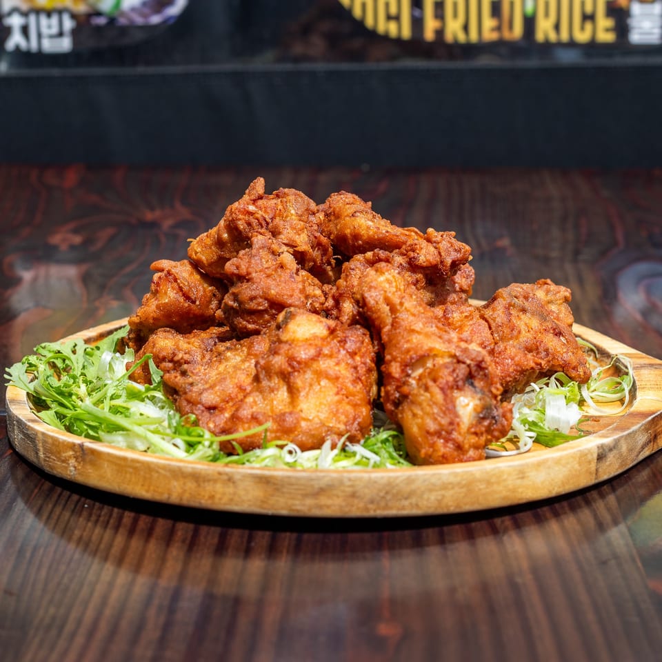 Crispy Korean fried chicken pieces on a wooden platter with fresh green lettuce and scallions.
