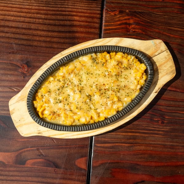 Korean corn cheese in an oval cast iron pan on a wooden serving board.