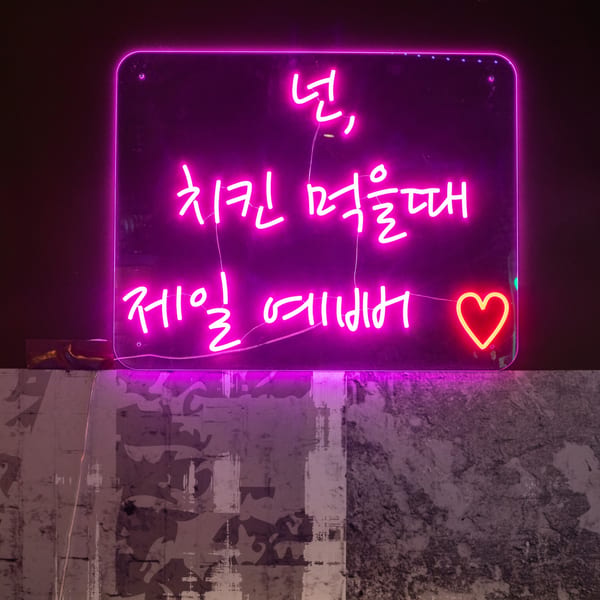 A bright pink neon sign with Korean text and a heart, mounted on a textured wall.