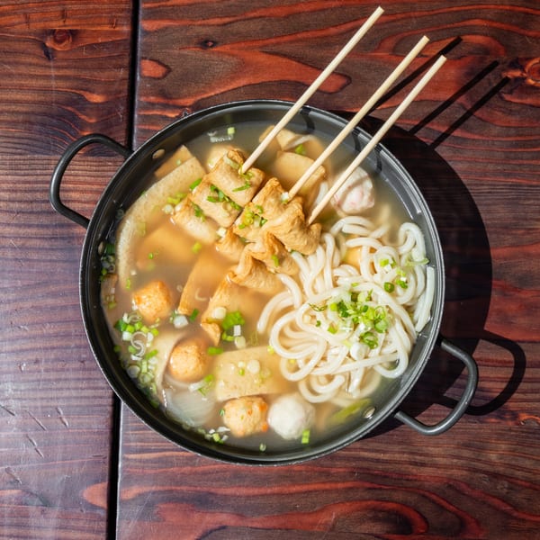 Overhead view of a hot pot with Korean fish cakes, udon noodles, and green onions.