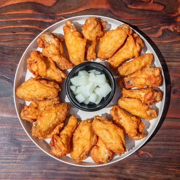 Golden-fried Korean chicken wings arranged in a circle around a bowl of pickled radish on a wooden table.